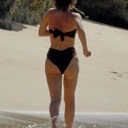 Emma Watson cu spatele într-un costum de baie negru din două piese pe plaja din Barbados