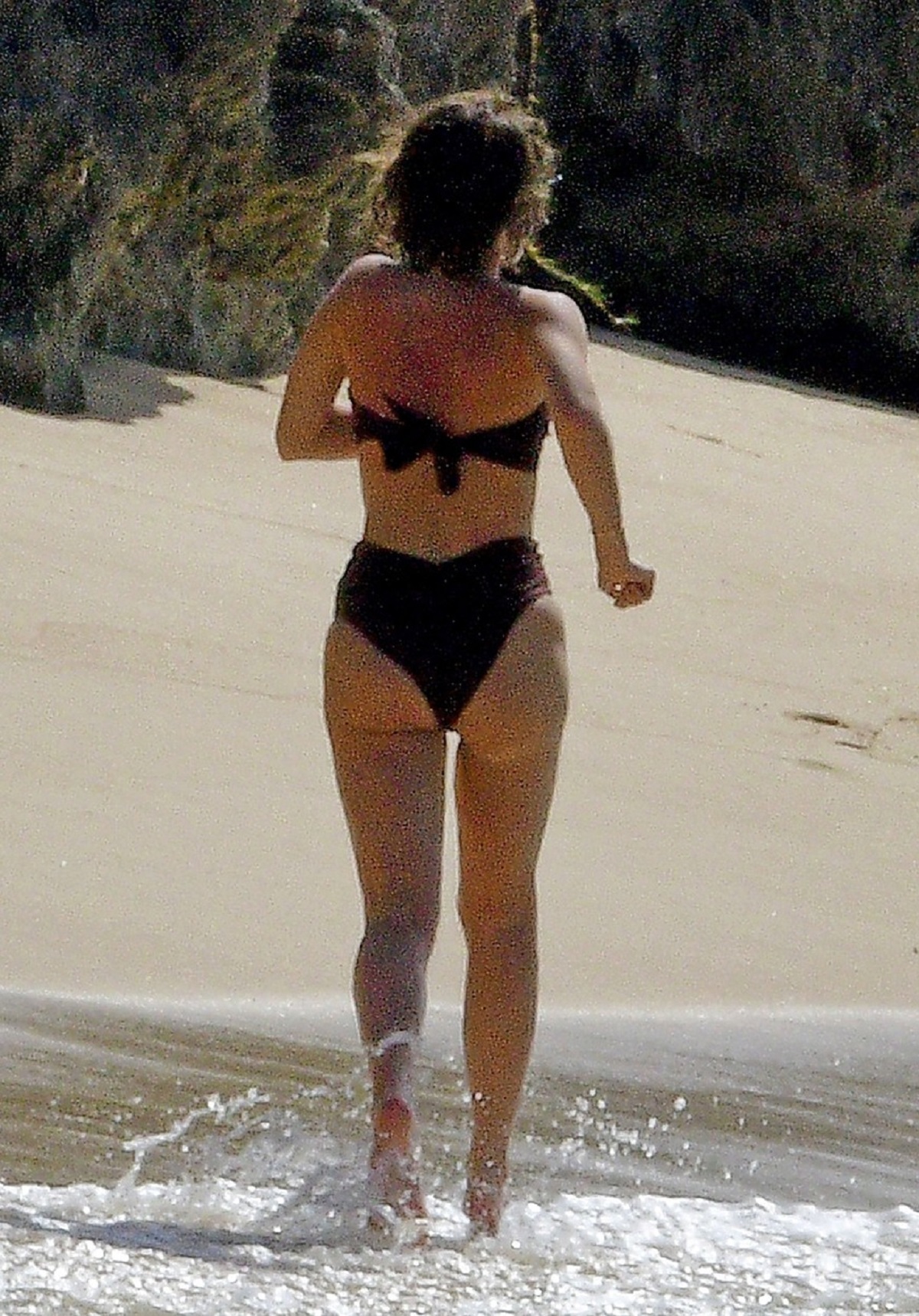 Emma Watson cu spatele într-un costum de baie negru din două piese pe plaja din Barbados