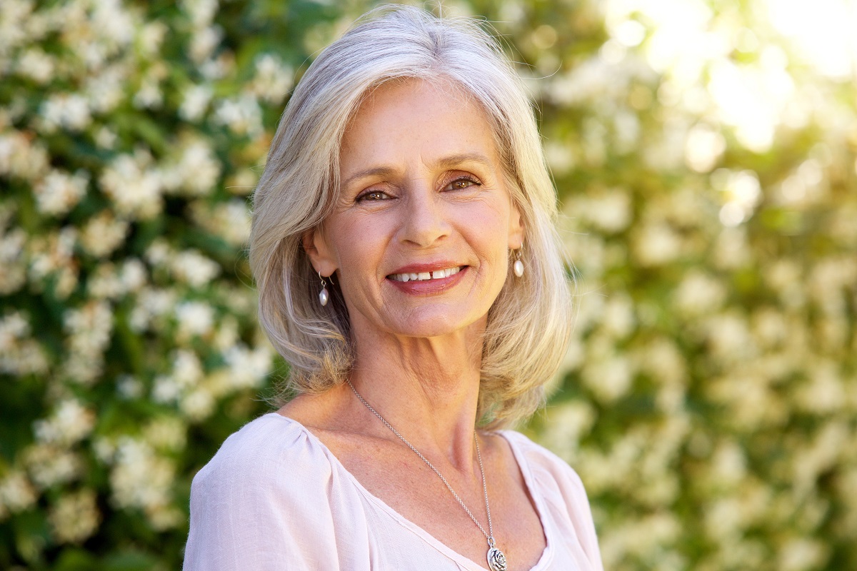 O femeie în vârstă cu părul alb care zâmbește pentru a indica unul din principalele obiceiuri la care e indicat să renunți după vârsta de 60 de ani