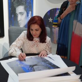 Priscilla Presley la o masă în timp ce semnează un autoportret realizat de Adam Rote