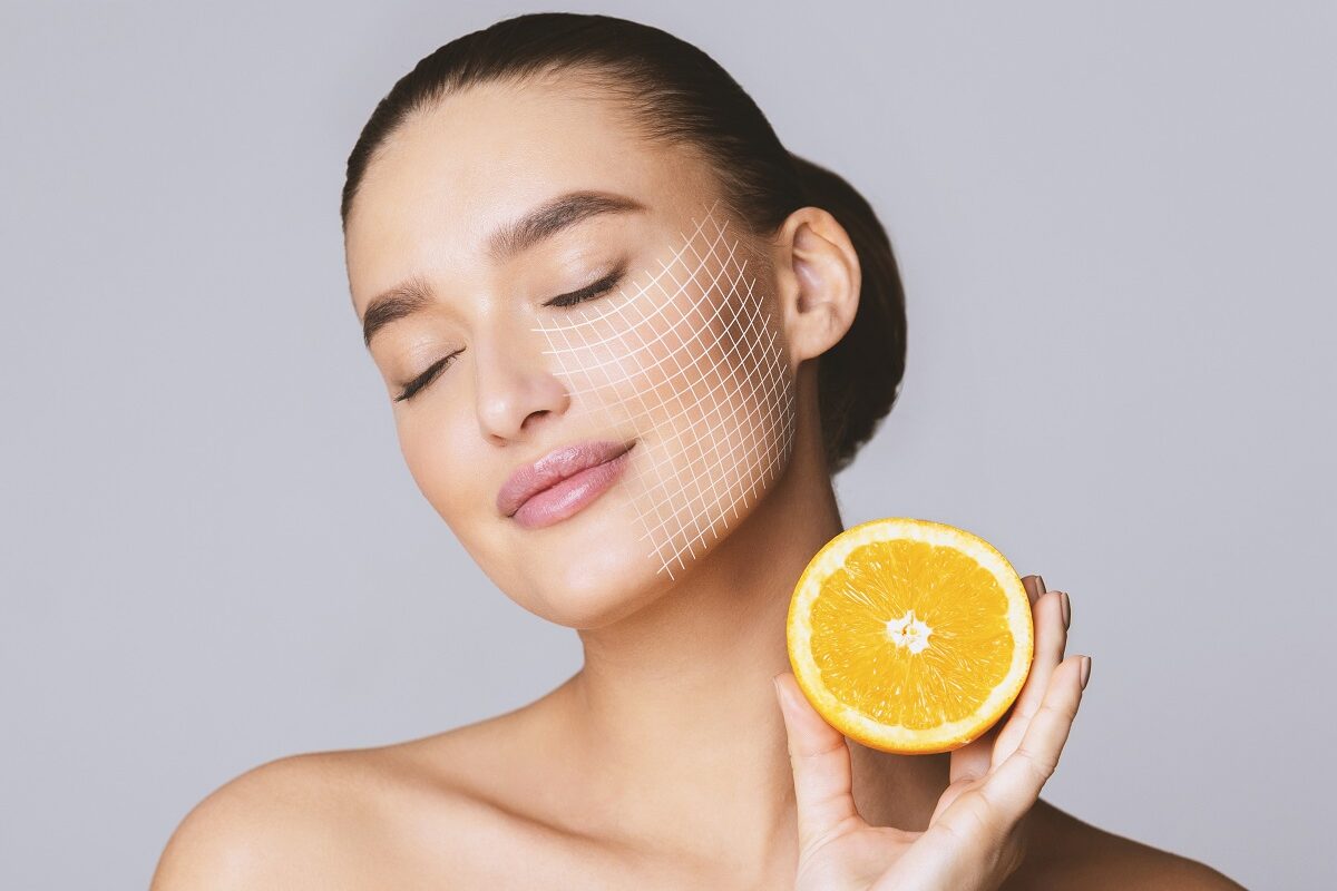 O femeie frumoasă cu tenul perfect care ține în mână o portocală pentru a ilustra principalele beneficii ale unui ingredient ca vitamina C pentru ten