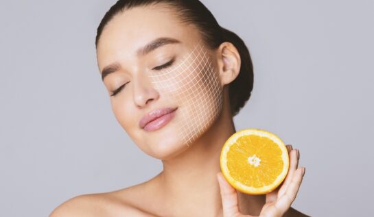 O femeie frumoasă cu tenul perfect care ține în mână o portocală pentru a ilustra principalele beneficii ale unui ingredient ca vitamina C pentru ten