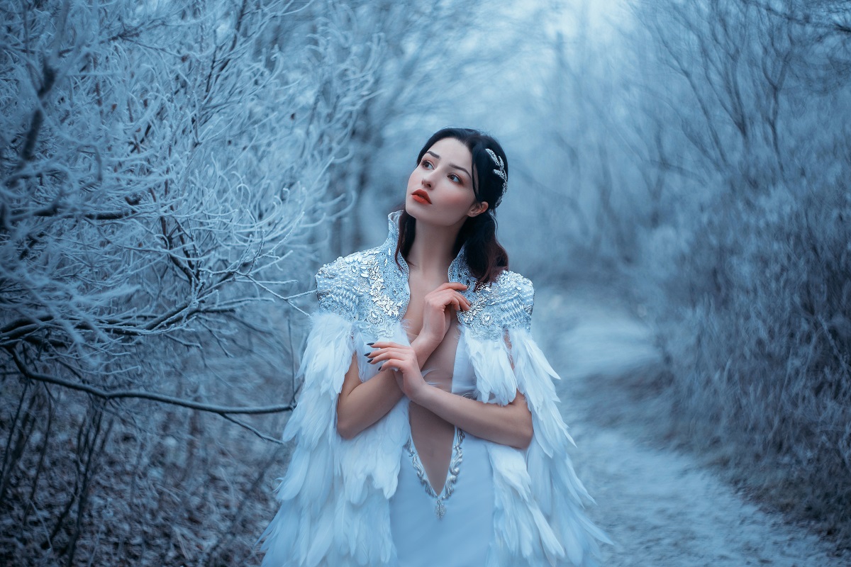O femeie frumoasă brunetă care poartă o rochie albă în timp ce stă într-o pădure înghețată pentru a reprezenta una dinc ele trei zodii ghinioniste în ziua de 10 decembrie 2021