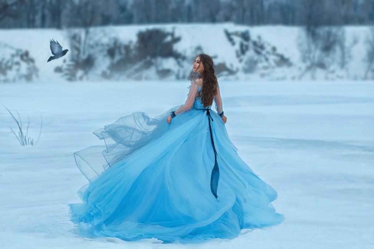 o femeie frumoasă într-o rochie albastră amplă care aleargă în zăpadă pentru a reprezenta una din zodiile ghinioniste în ziua de 8 decembrie 2021