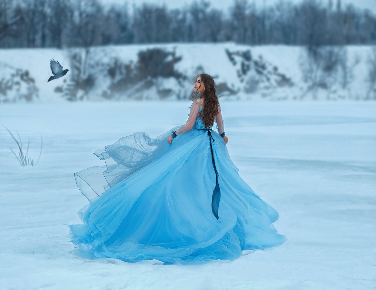 o femeie frumoasă într-o rochie albastră amplă care aleargă în zăpadă pentru a reprezenta una din zodiile ghinioniste în ziua de 8 decembrie 2021
