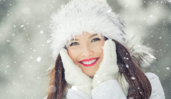 O femeie frumoasă cu o căciulă de iarnă albă în timp ce stă în zăpadă pentru a reprezenta una din cele trei zodii norocoase în ziua de 18 decembrie 2021