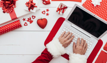 O femei care tastează la un laptop alb, pe un fundal cu decorațiuni de Crăciun