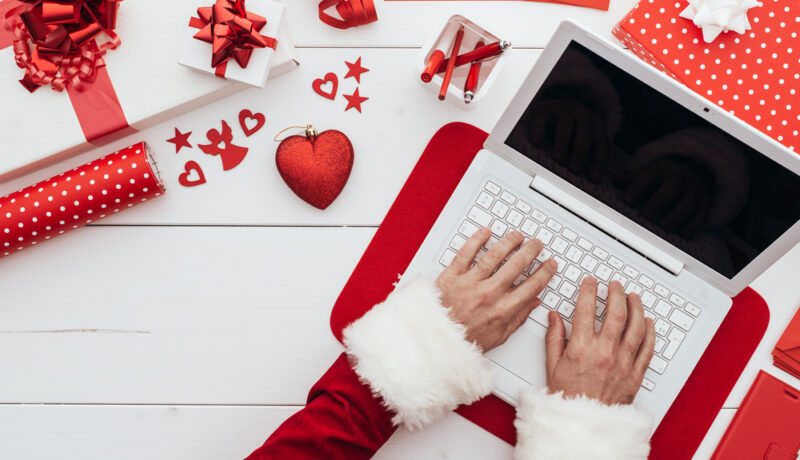 O femei care tastează la un laptop alb, pe un fundal cu decorațiuni de Crăciun