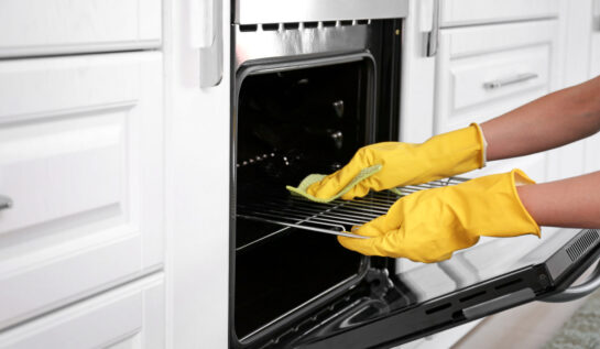 O femeie cu mănuși de protecție de culoare galebenă curăță un cuptor electric.