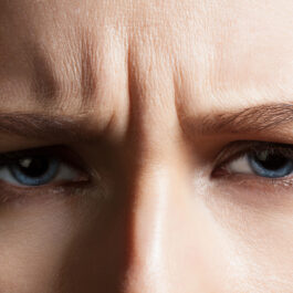 O femeie cu ochii albaști care stă încruntată și face ridurile de expresie dintre sprâncene