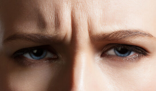 O femeie cu ochii albaști care stă încruntată și face ridurile de expresie dintre sprâncene