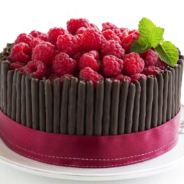 Tort de ciocolată cu zmeură, decorat cu sticksuri de ciocolată și înconjurat cu bandă roșie
