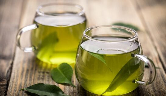 O masă pe care se află două cești transparente cu ceai pentru a ilustra beneficiile ceaiului verde