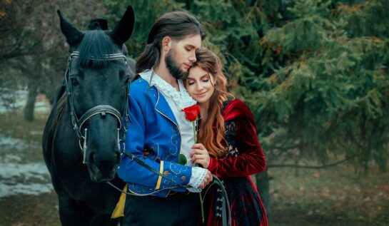 Un cuplu de îndrăgostiți în timp ce stau îmbrățișați lângă un cal negru
