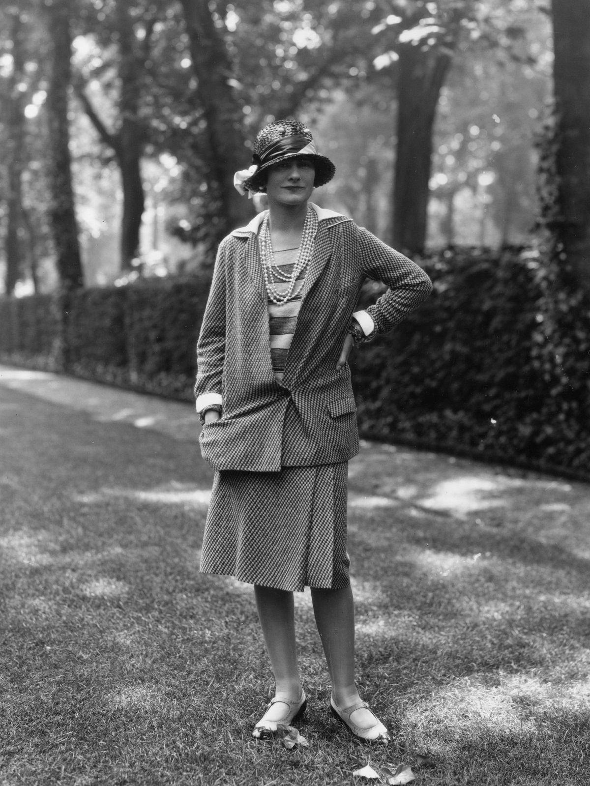 Coco Chanel cu o mână în șold în timp ce poartă o creație proprie