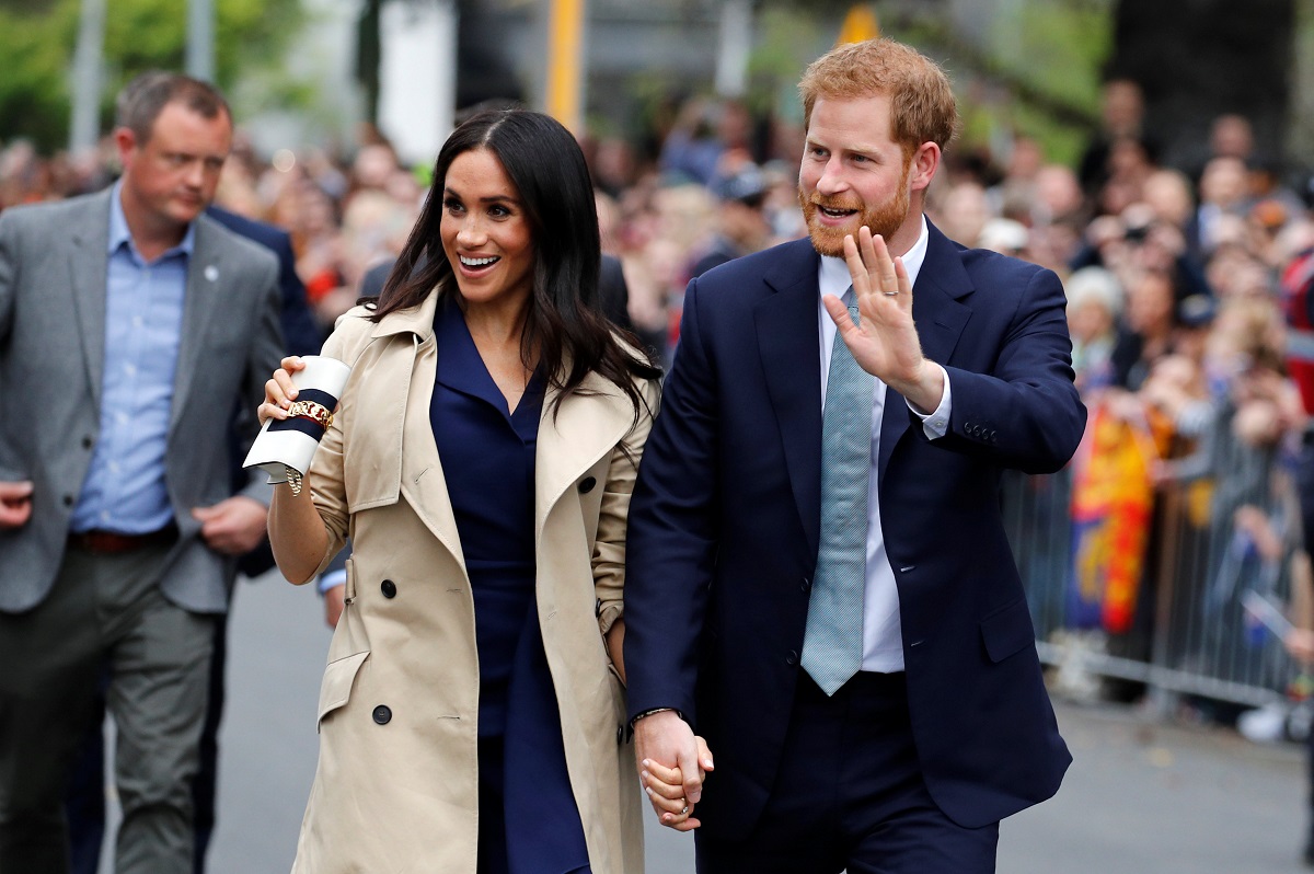 Meghan Markle și Prințul Harry în timp ce se țin de mână și salută publicul înc adrul unei întâlniri oficiale din Regatul Unit