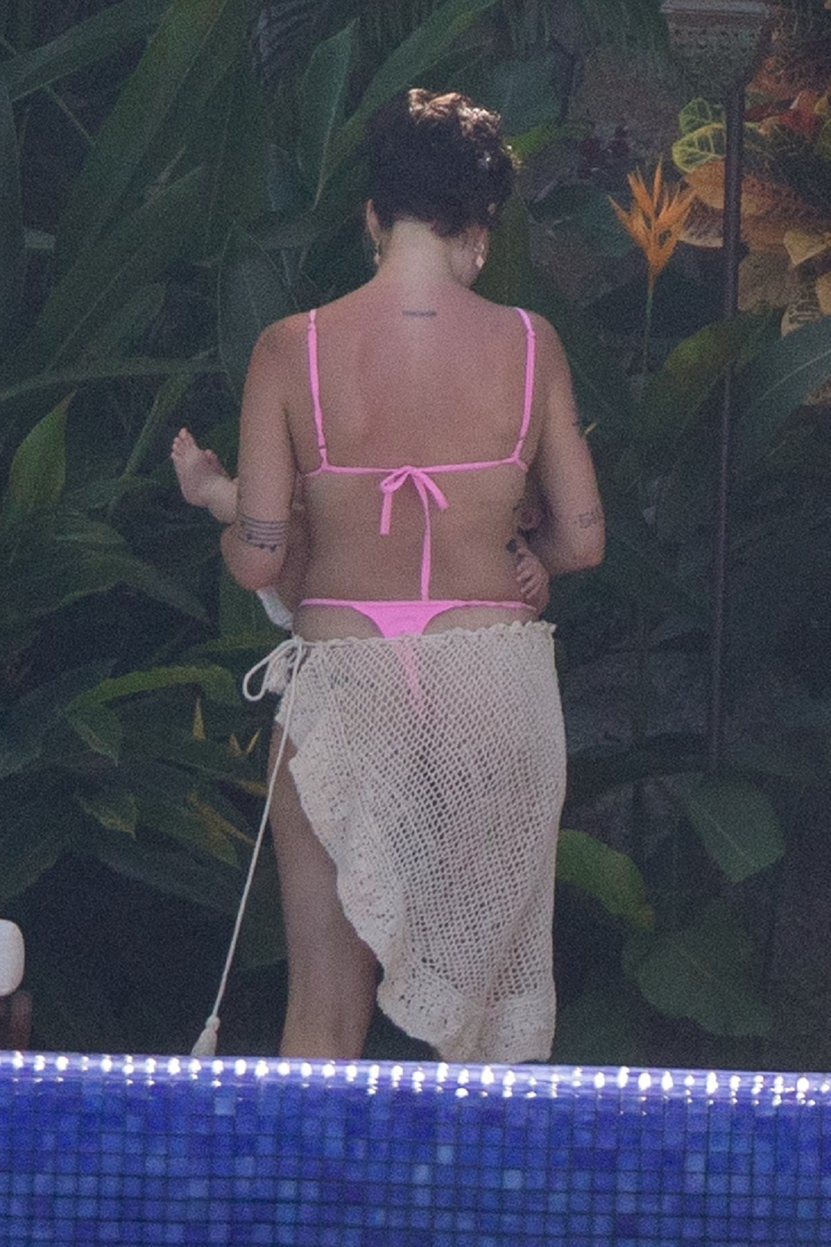 Halsey într-un costum de baie roz în timp ce stă cu spatele și își ține în brațe copilul
