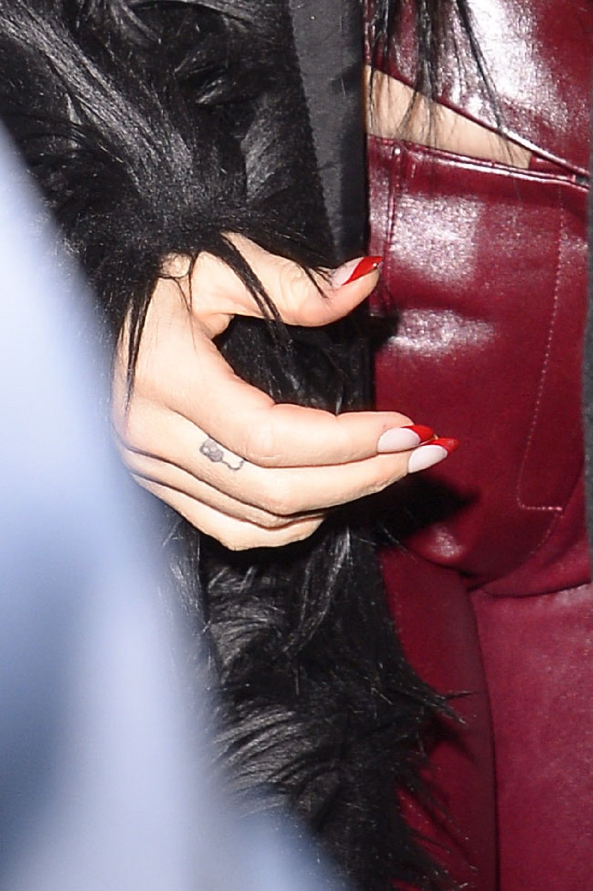 Katy Perry, într-un costum din piele burgundy, în timp ce își lasă la vedere un tataj mic de pe degetul mâiniii