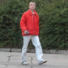 Lykke Li, într-o geacă roșie și o pereche de pantaloni de trening gri în timp ce se plimbă prin cartier