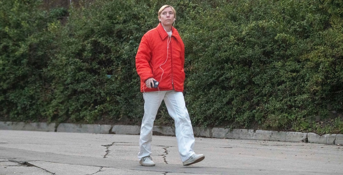 Lykke Li, într-o geacă roșie și o pereche de pantaloni de trening gri în timp ce se plimbă prin cartier