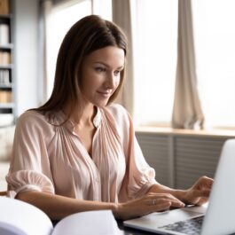 O femeie frumoasă care poartă o bluză din satin roz și scrie la laptop câteva obiceiuri sănătoase pentru anul 2022