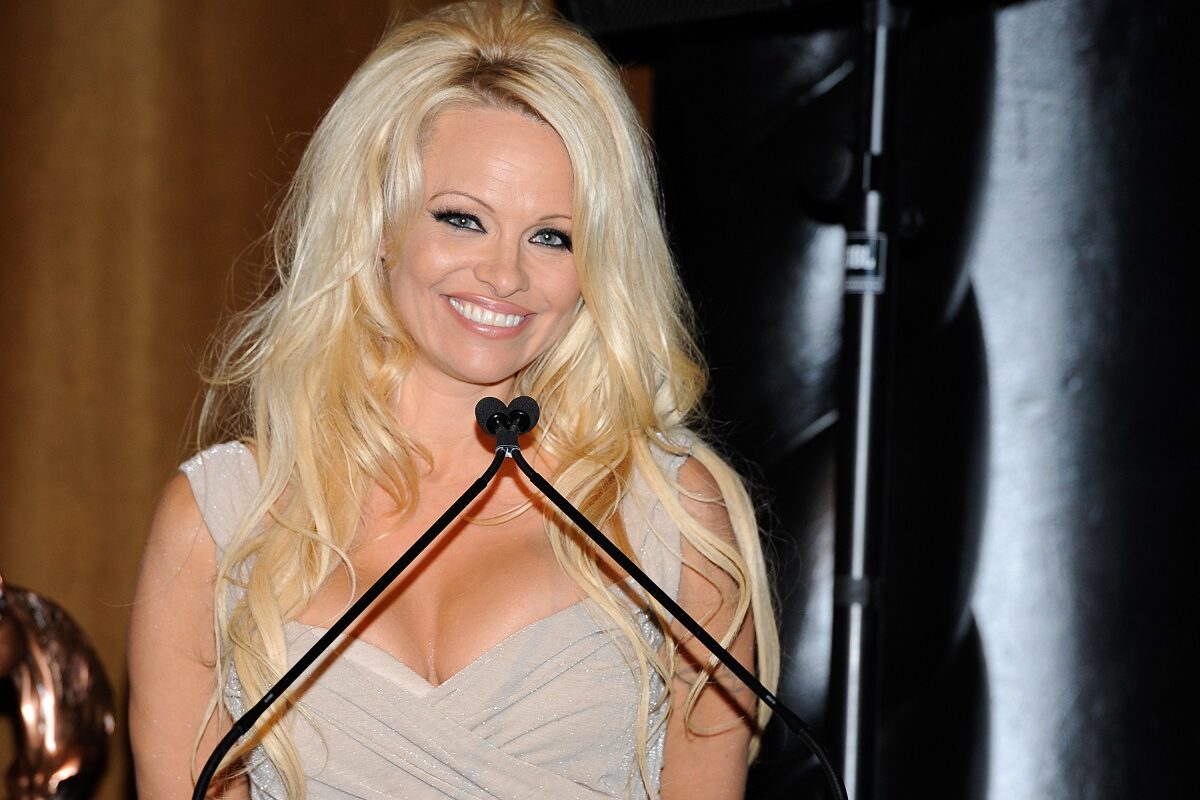 Pamela Anderson într-un top alb cu decolteu adânc în timp ce vorbește în fața unui pupitru la un eveniment public