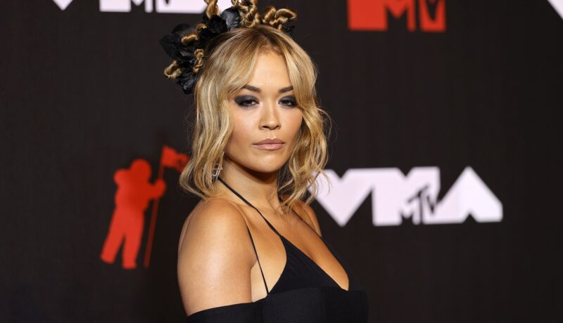 Rita Ora cu părul prins și într-o rochie neagră în timp ce pozează pe covorul roșu la Gala MTV VMA din anul 2021