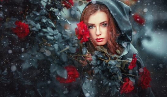 O femeie frumoasă care poartă o pelerină neagră și stă lângă un gard de trandafiri roșii pentru a reprezenta una din cele trei zodii ghinioniste în ziua de 14 ianuarie 2022