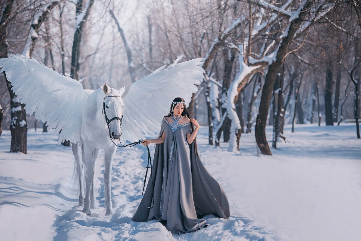 o femeie frumoasă într-o rochie argintie în timp ce plimbă un cal alb cu aripi prin pădure pentru a reprezenta una din cele trei zodii norocoase în ziua de 13 ianuarie 2022