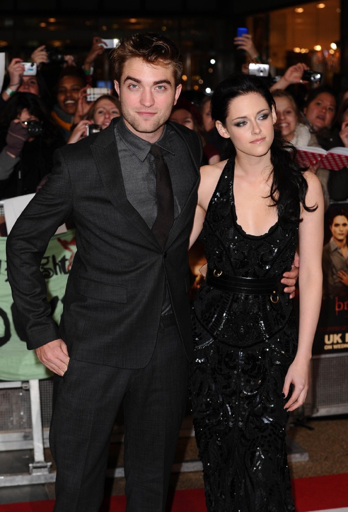 Kristen Stewart într-o rochie neagră alături de actorul Robert Pattinson care este la costum, în timp ce pozează pe covorul roșu la premiera filmului Twilight din Londra