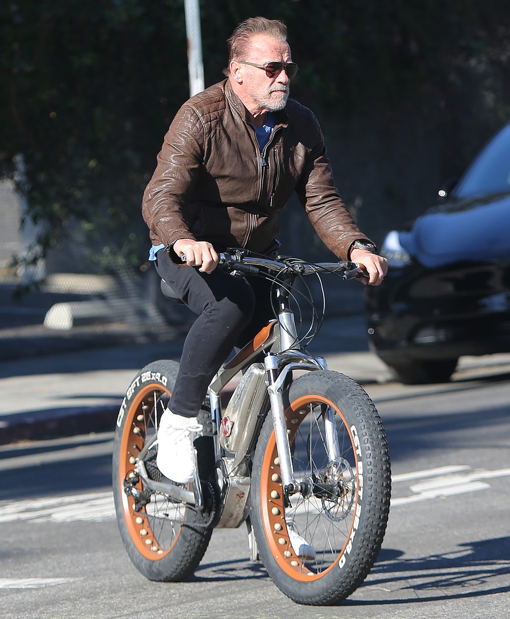 Arnold Schwarzenegger, îmbrăcat într-o haină din piele, pe bicicletă