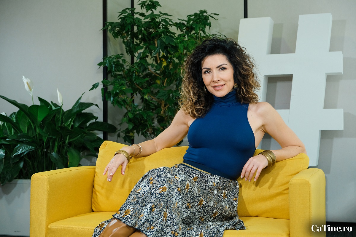 Carmen Brumă într-un top albastru și o fustă cu imprimeu în timp ce stă pe o canapea galbenă la interviul pentru CaTine.ro