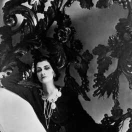 Coco Chanel într-o rochie neagră în timp ce stă întinsă pe o canapea