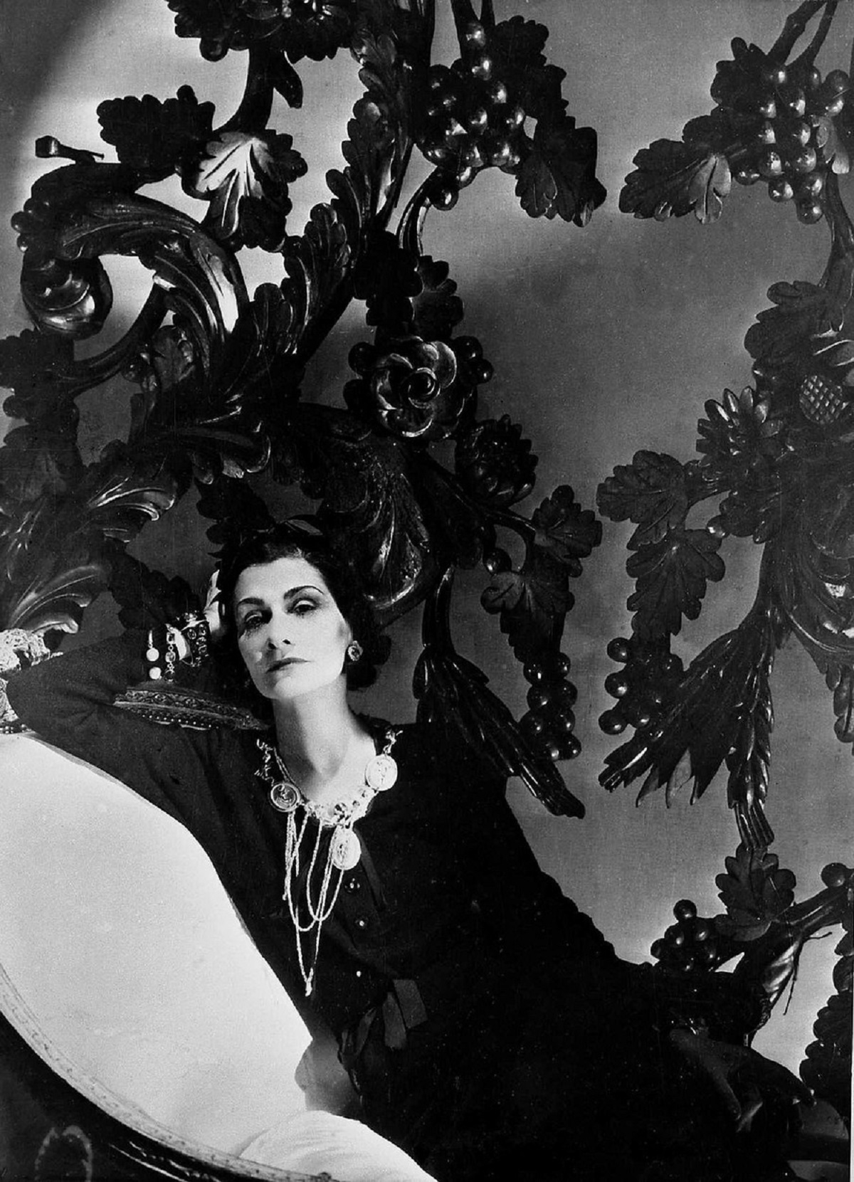 Coco Chanel într-o rochie neagră în timp ce stă întinsă pe o canapea