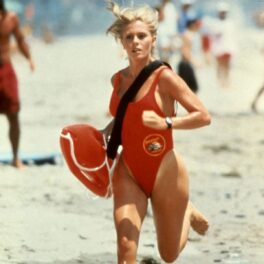 Nicole Eggertîn timp ce aleargă pe plajă într-un costum de baie roșu în serialul Baywatch