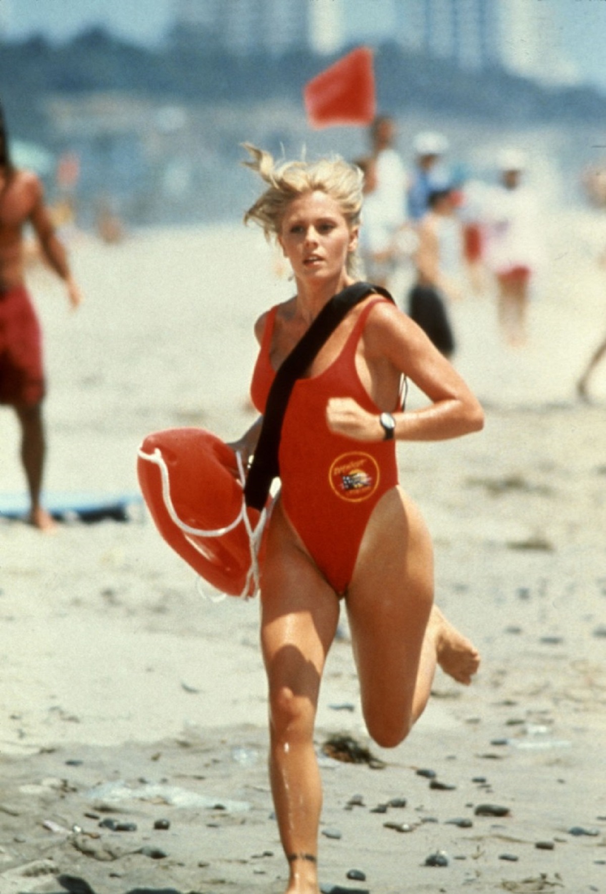 Nicole Eggertîn timp ce aleargă pe plajă într-un costum de baie roșu în serialul Baywatch