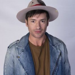Radu Vâlcan, cu pălărie pe cap, poză la panou