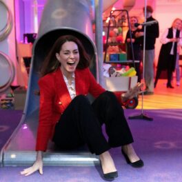 Kate Middleton într-un sacou roșu și o pereche de pantaloni negri în timp ce se dă pe un tobogan