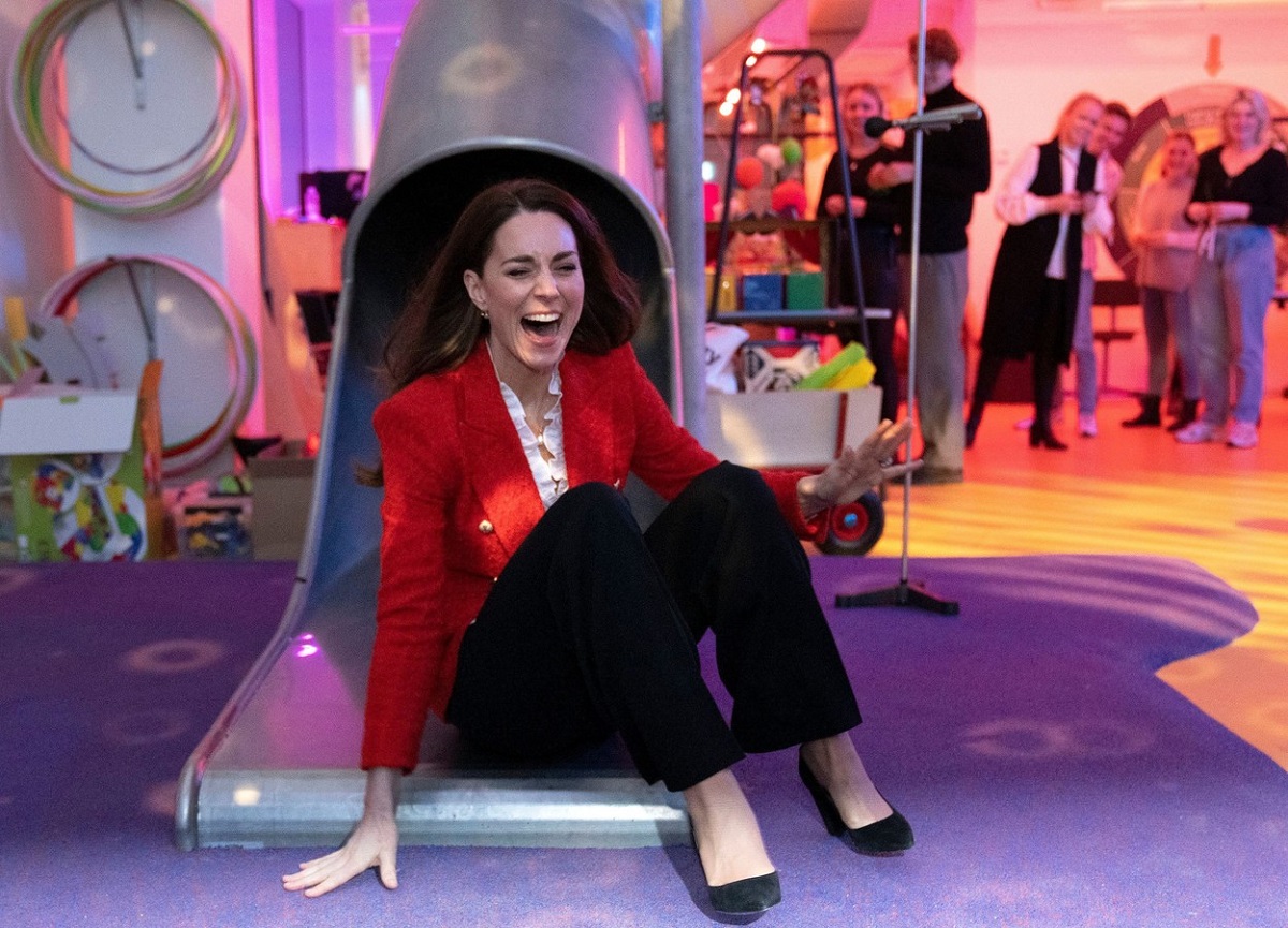 Kate Middleton într-un sacou roșu și o pereche de pantaloni negri în timp ce se dă pe un tobogan