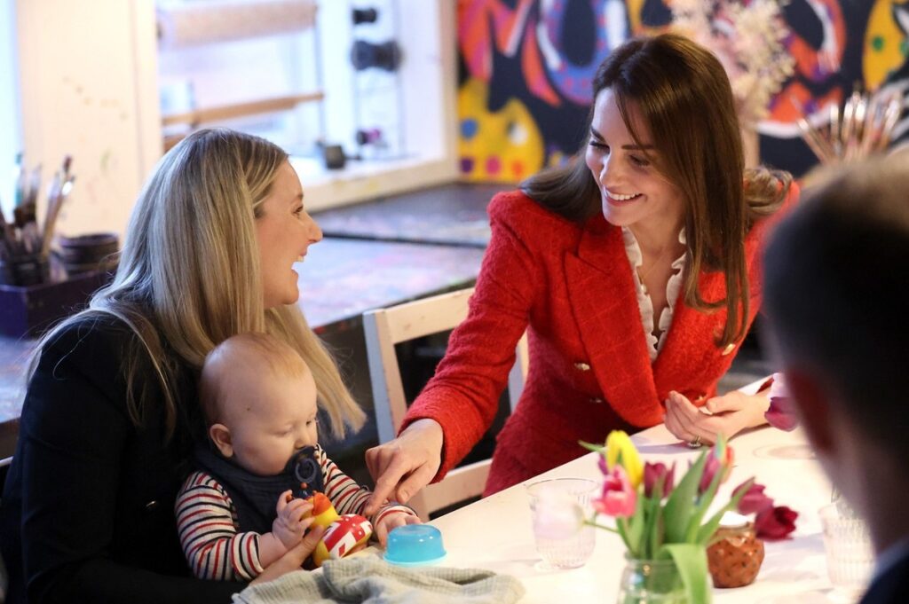 Kate Middleton îmbrăcată într-un sacou roșu în timp ce stă de vorbă cu o mămică și fiul acesteia în cadrul turului regal din Danemarca