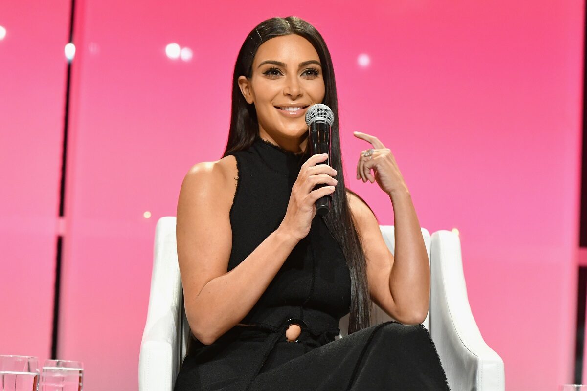Kim Kardashian într-o ținută neagră în timp ce stă pe un scaun și vorbește la un microfon