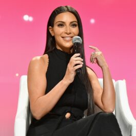Kim Kardashian într-o ținută neagră în timp ce stă pe un scaun și vorbește la un microfon