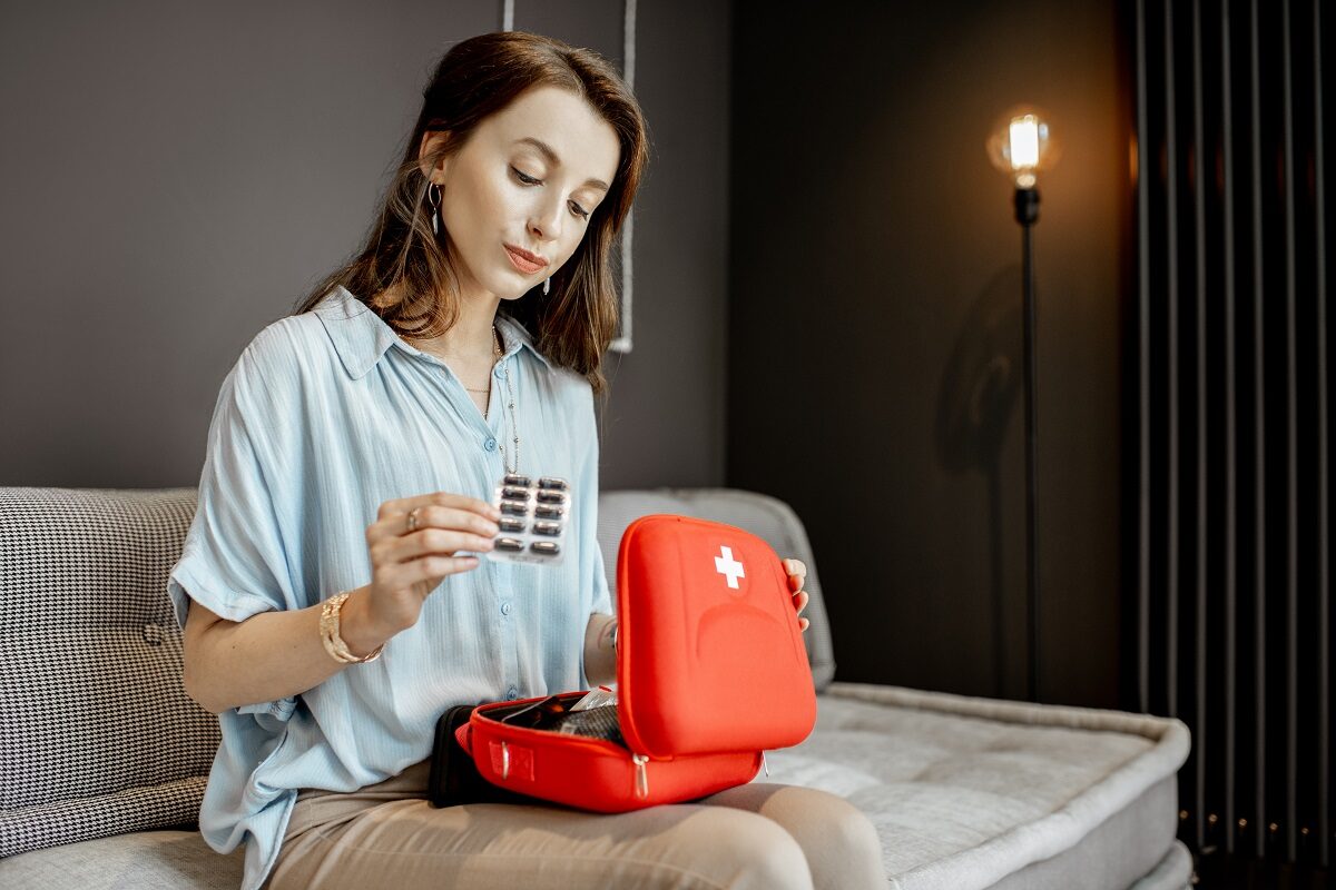O femeie frumoasă care stă pe pat și pune pastile într-un kit roșu de prim ajutor