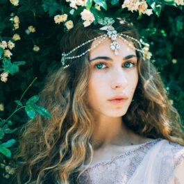 O fată frumoasă stă printre flori și poartă o coroniță de flori în păr