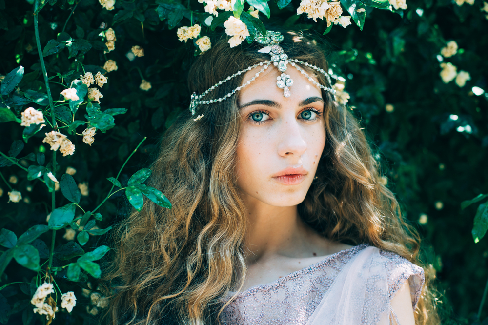 O fată frumoasă stă printre flori și poartă o coroniță de flori în păr