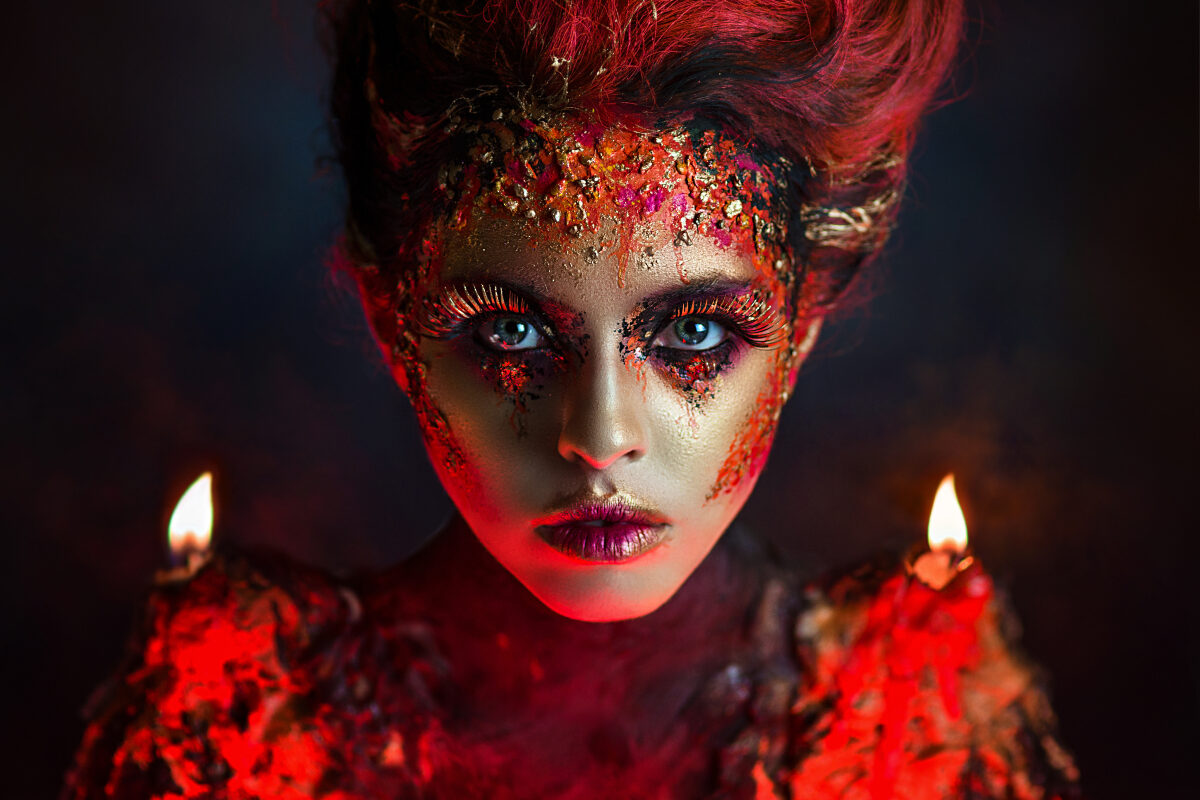 O femeie frumoasă, cu ochi albaștri, machiată în nuanțe de roșu și auriu, pentru a ilustra zodii cu un temperament vulcanic