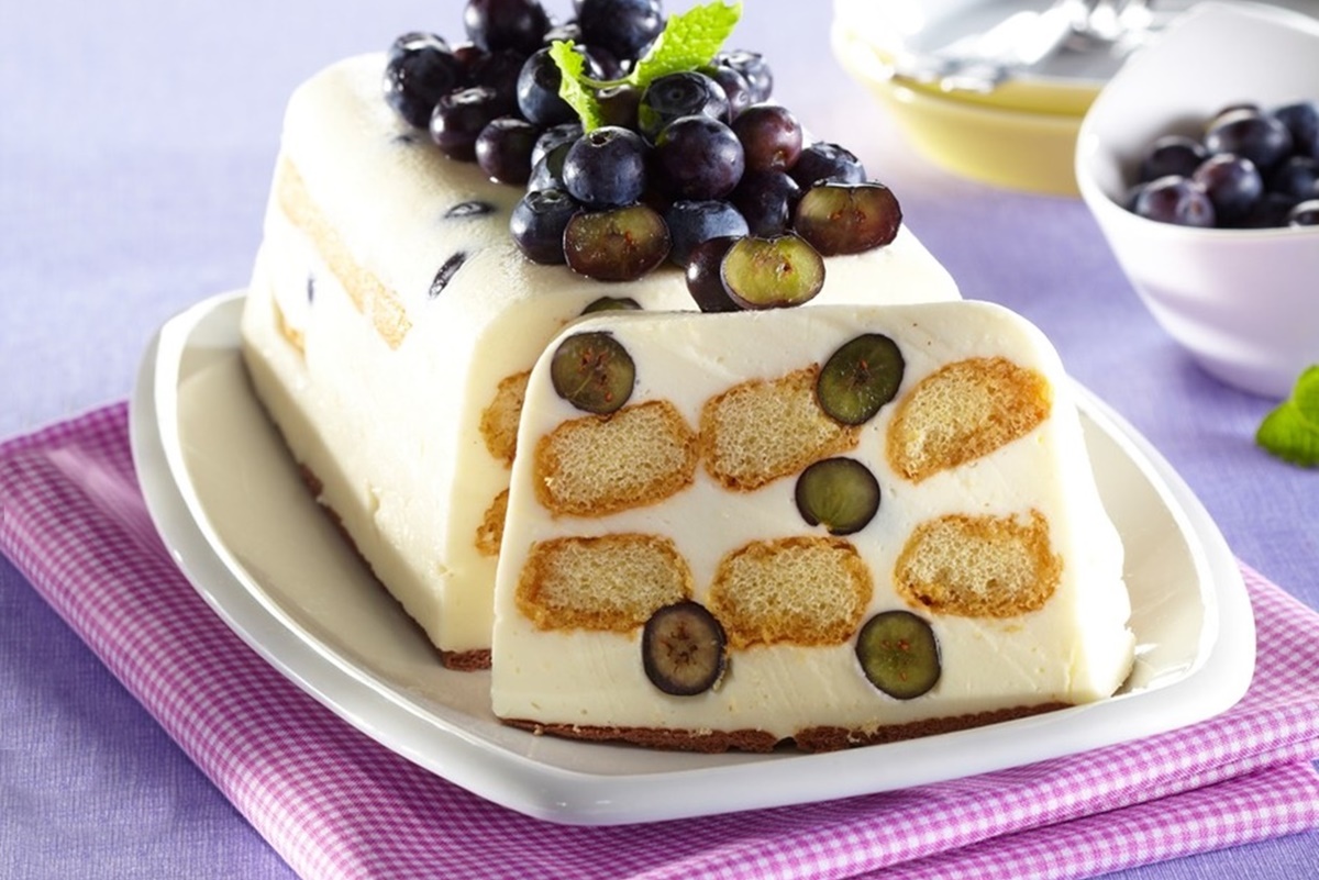 Prăjitură din pișcoturi cu cremă de mascarpone și afine porționată pe un platou alb