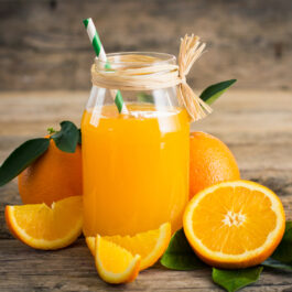 Suc de portocale, într-un pahar transparent, pus pe un blat din lemn