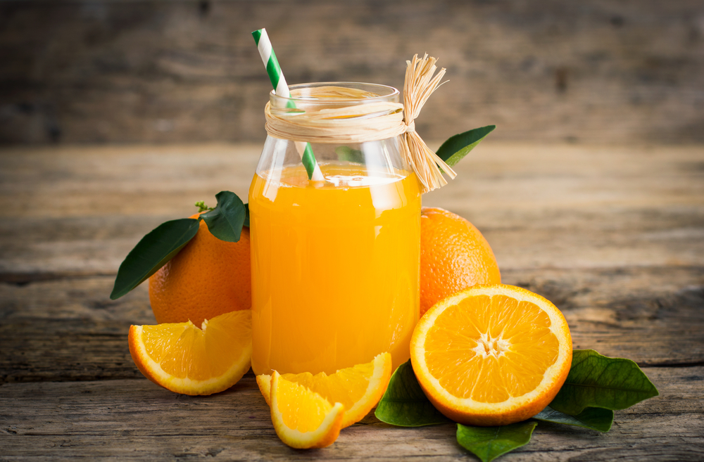 Suc de portocale, într-un pahar transparent, pus pe un blat din lemn