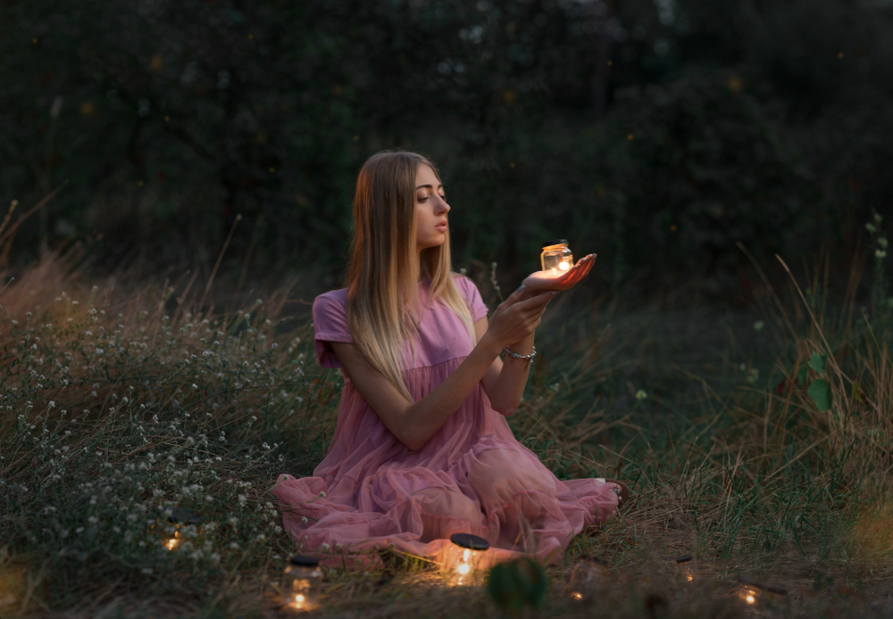 O fată stă pe iarbă și ține o lumină în palme